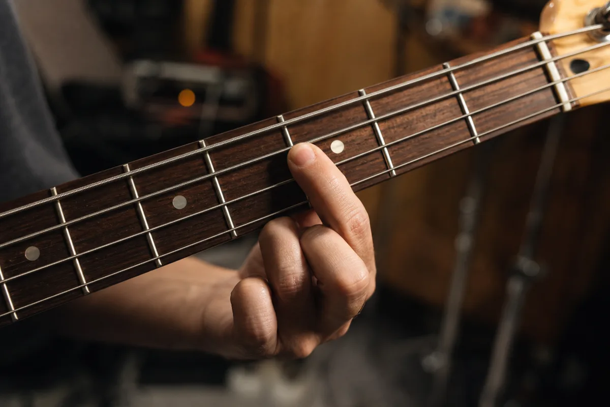 Main gauche d’un bassiste posant la fondamentale sur le manche