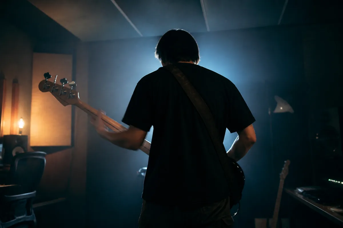 Bassiste de dos jouant en slap sur une basse electrique dans un studio